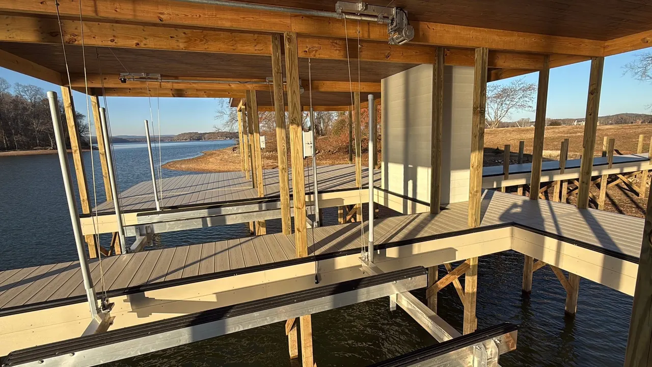 Inside a newly built covered dock with boat lifts at golden hour, the lake and shoreline behind it
