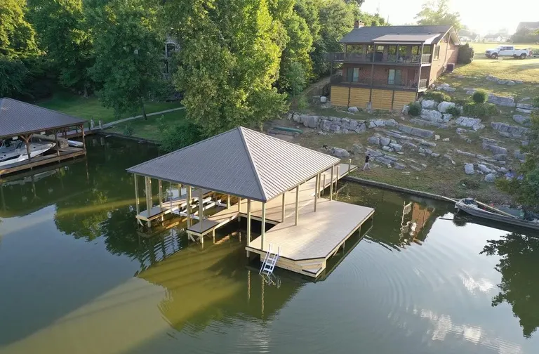 Aerial view of a covered dock with a swim platform below a lakeside home